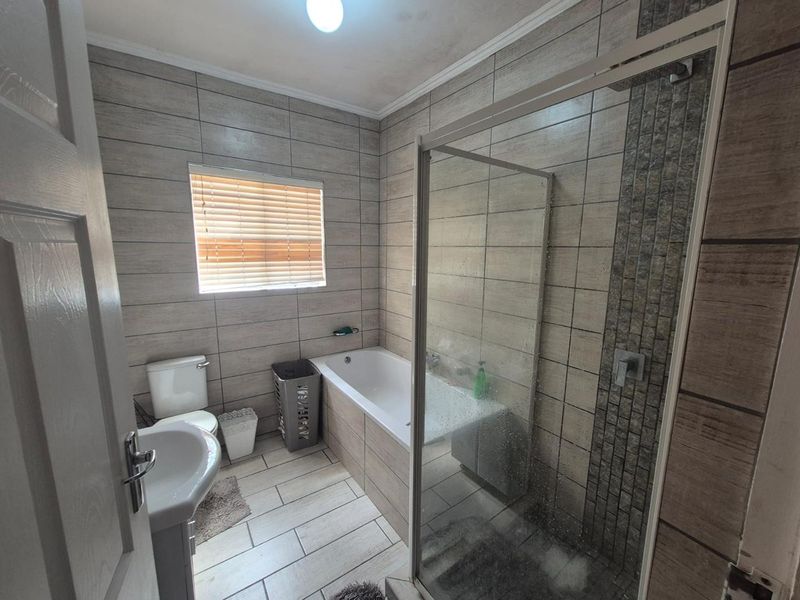 A modern bathroom featuring a glass-enclosed shower, a bathtub, a pedestal basin, and a toilet, finished with neutral-toned wall and floor tiles.