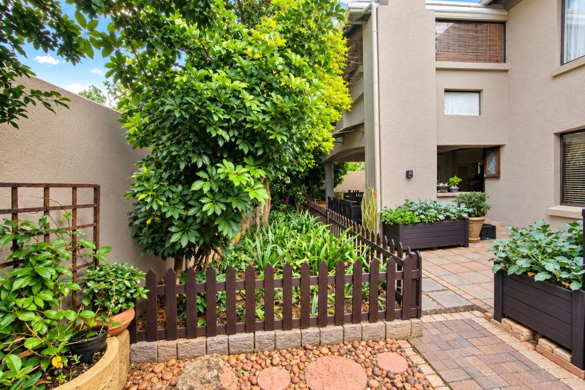 A well-maintained rear courtyard featuring paved pathways, established garden beds with timber fencing, and a private patio area adjacent to the townhouse structure.