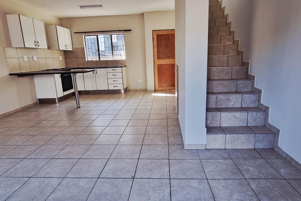 Open-plan living area featuring tiled flooring, a functional kitchen with built-in cabinetry and oven, and a staircase leading to the upper level.