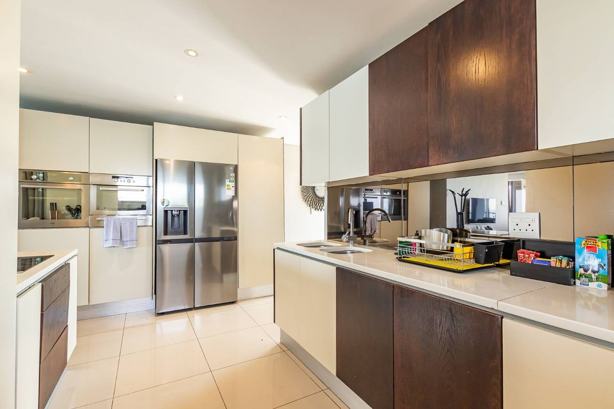 Modern kitchen featuring two-tone cabinetry, stone countertops, integrated stainless steel appliances, and a mirrored backsplash, offering a sleek and functional culinary space.