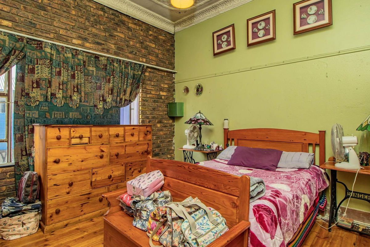 A bedroom featuring a rustic exposed brick feature wall, decorative ceiling cornice, and timber flooring.
