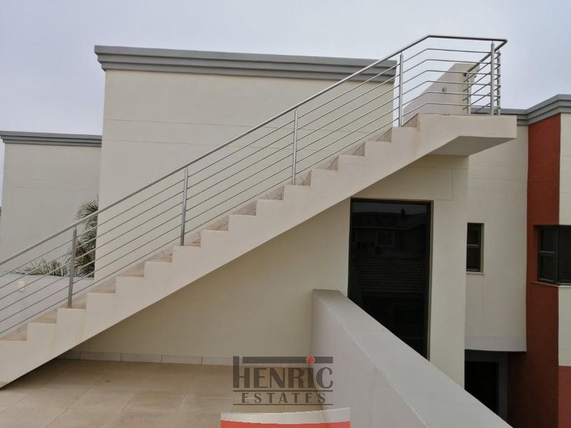 Exterior view of a modern home featuring an external staircase with stainless steel balustrades leading to an upper level, set against a tiled patio area.