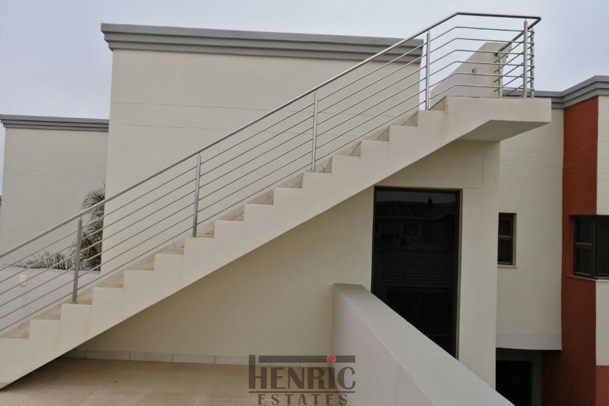 Exterior view of a modern home featuring an external staircase with stainless steel balustrades leading to an upper level, set against a tiled patio area.