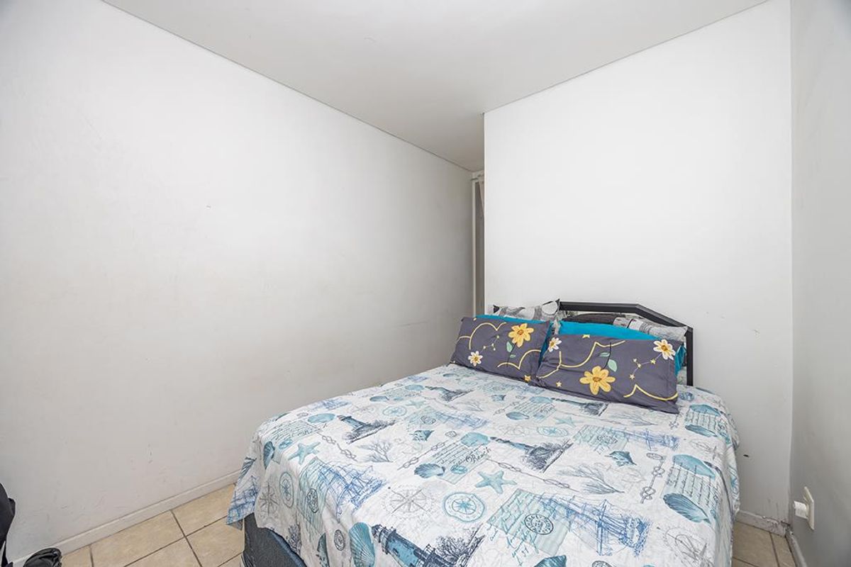 A compact bedroom featuring tiled flooring and plain white walls, offering a neutral space ready for personalization or renovation.