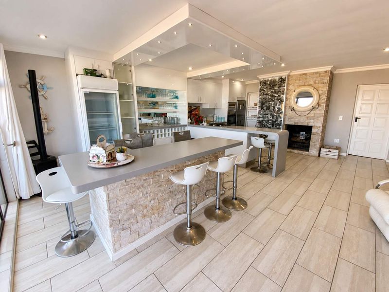 Spacious open-plan living and kitchen area featuring a stone-clad breakfast bar, built-in fireplace, and modern recessed ceiling lighting.