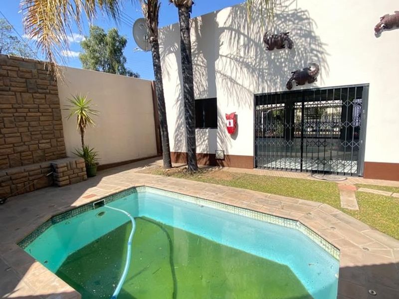 Outdoor pool area featuring stone cladding, security gate, and fire safety equipment, currently requiring maintenance to the pool water.