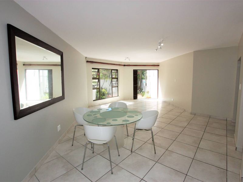 A bright and spacious living area featuring neutral tiled flooring, large aluminium windows, and sliding glass doors providing access to the exterior.