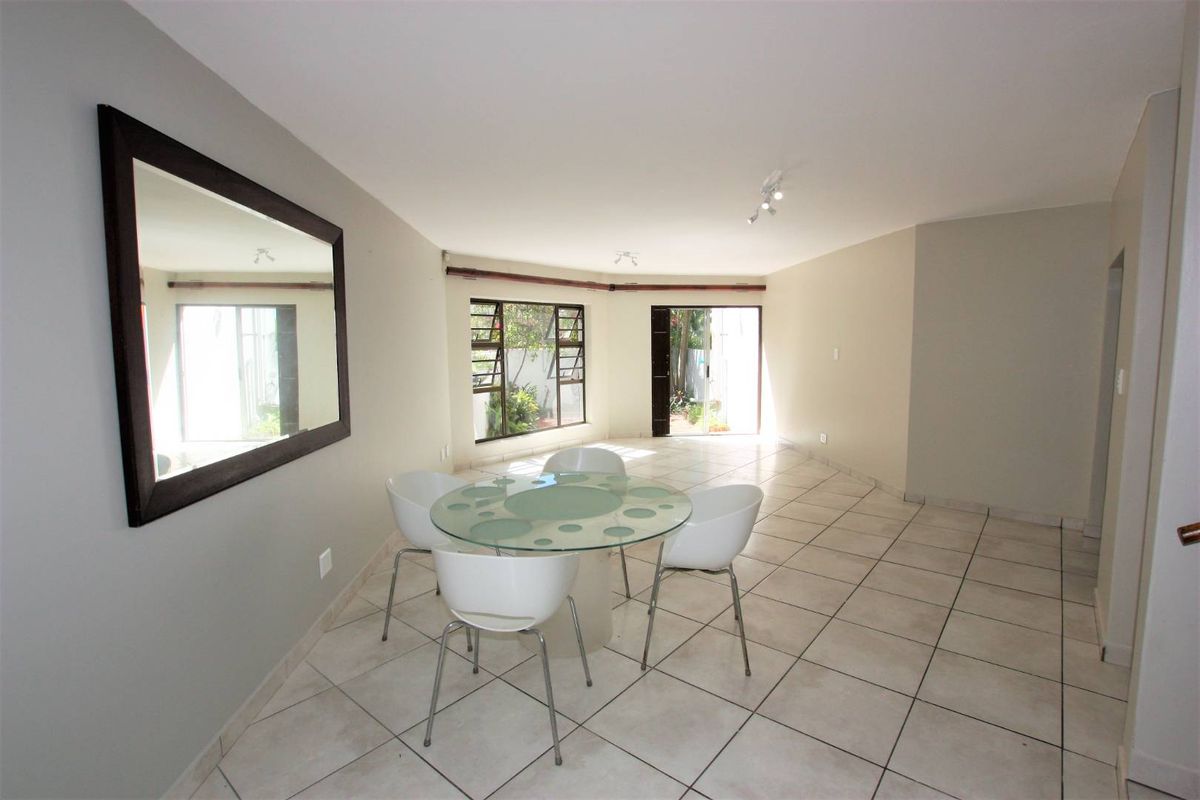 A bright and spacious living area featuring neutral tiled flooring, large aluminium windows, and sliding glass doors providing access to the exterior.