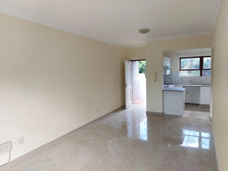 An open-plan living area featuring tiled flooring and a connected kitchen space, offering a clean, neutral canvas for potential interior design updates.