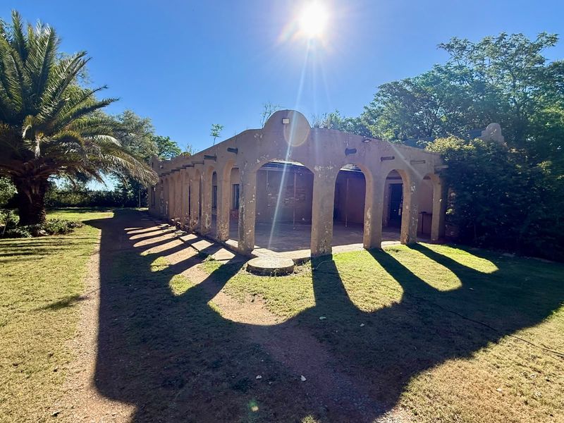 A rear view of the property featuring a covered patio with a distinctive arched colonnade, set within a spacious garden area.