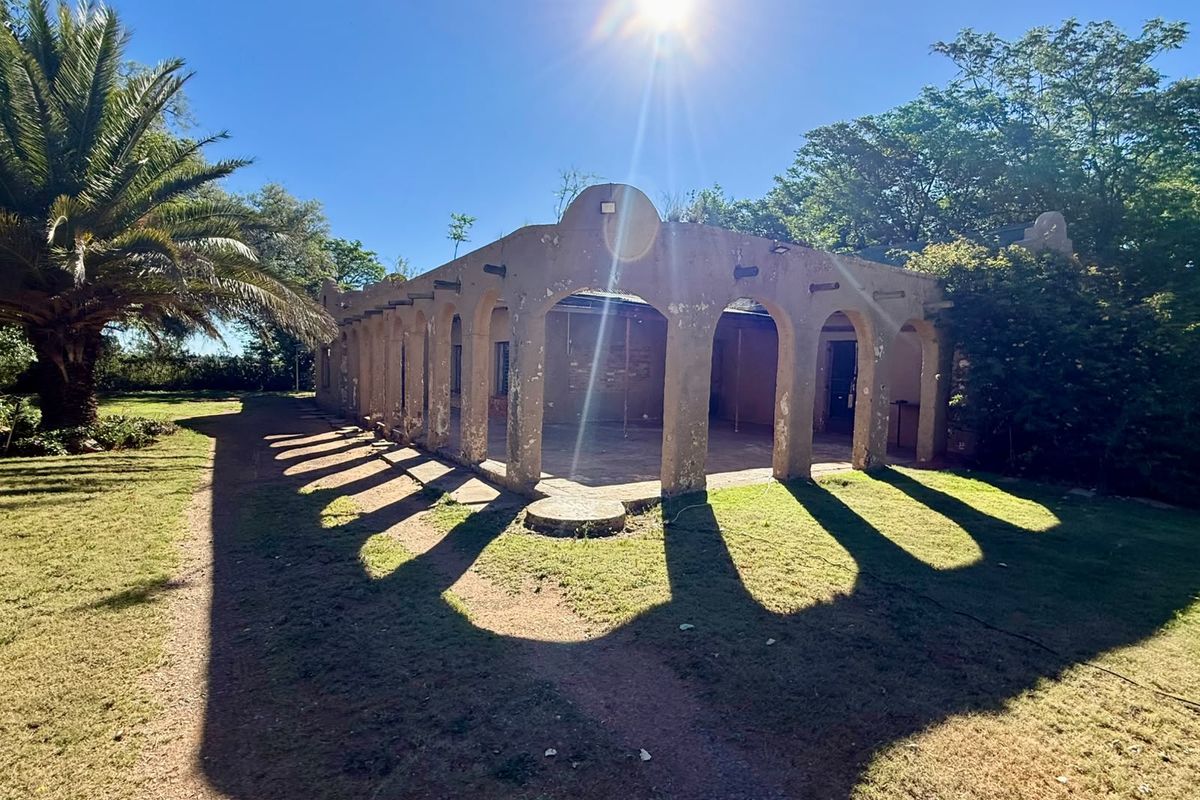 A rear view of the property featuring a covered patio with a distinctive arched colonnade, set within a spacious garden area.