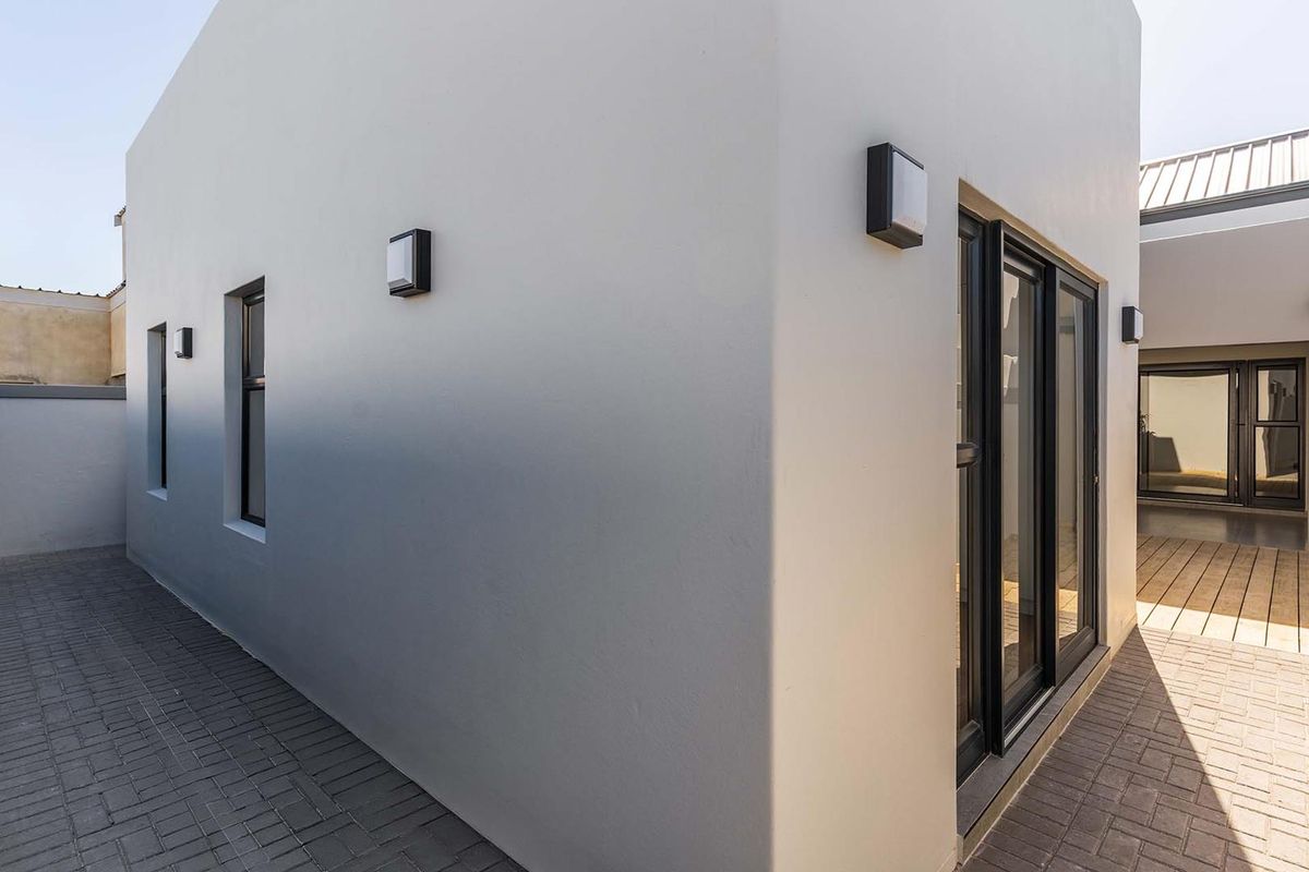 A modern exterior rear courtyard featuring paved walkways, timber decking, and contemporary aluminium sliding doors with integrated wall lighting.