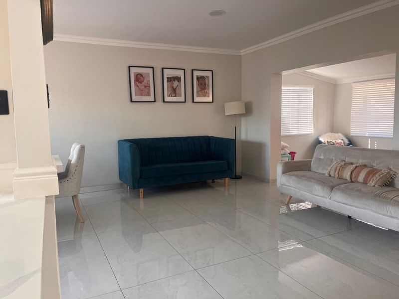 A bright and spacious living area featuring polished tiled flooring, crown molding, and large windows fitted with venetian blinds.
