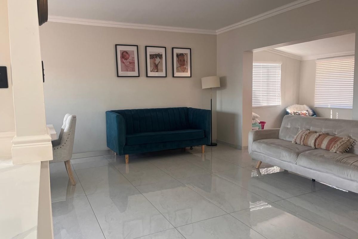 A bright and spacious living area featuring polished tiled flooring, crown molding, and large windows fitted with venetian blinds.