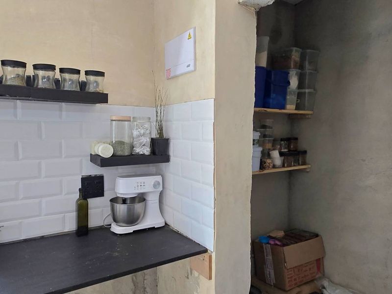 A scullery or pantry area featuring a subway tile backsplash, dark countertop, and open shelving, currently requiring wall finishing and plastering.