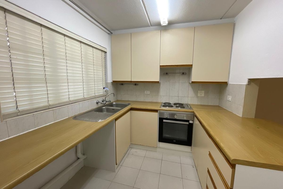 A functional kitchen featuring laminate countertops, built-in oven, electric cooktop, and tiled splashback, offering a clean and practical workspace.
