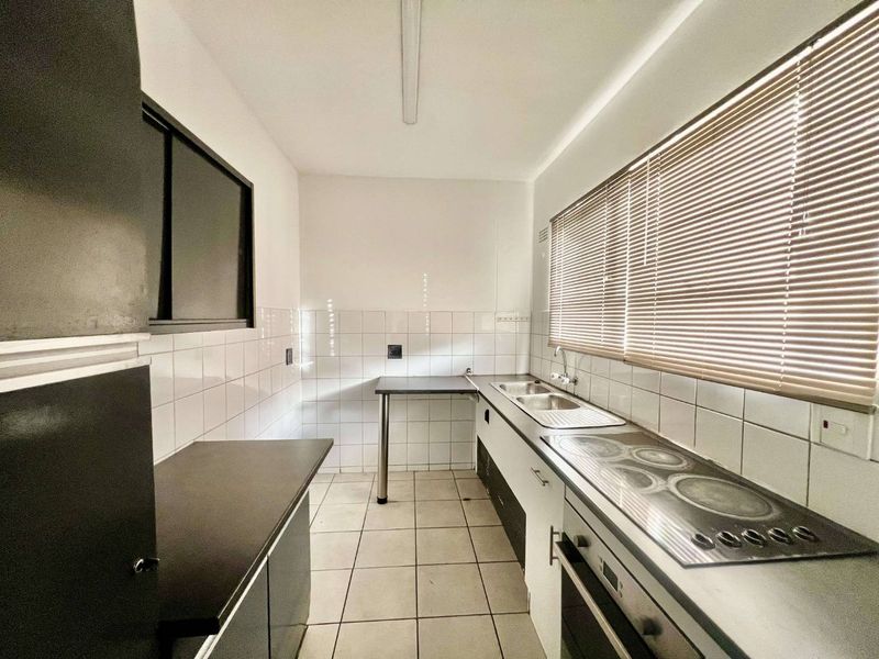 A functional, empty kitchen featuring built-in cabinetry, a stainless steel double sink, an integrated electric hob and oven, and tiled flooring.