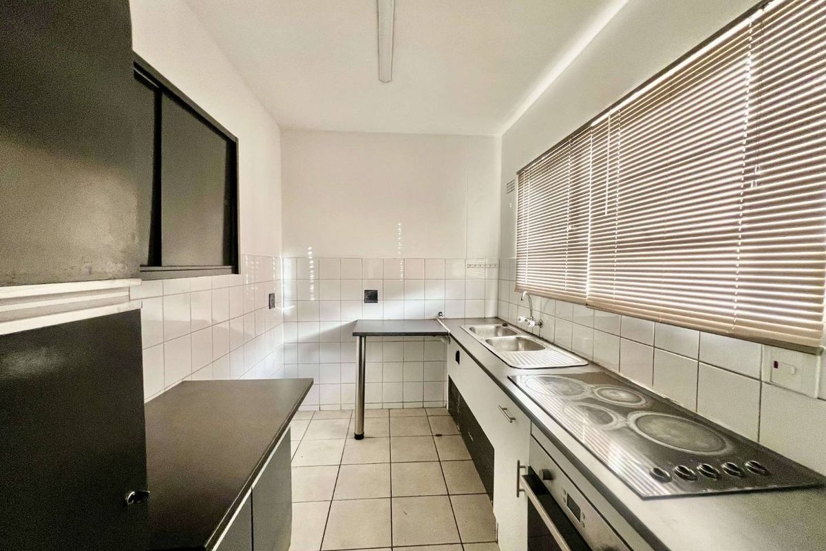 A functional, empty kitchen featuring built-in cabinetry, a stainless steel double sink, an integrated electric hob and oven, and tiled flooring.