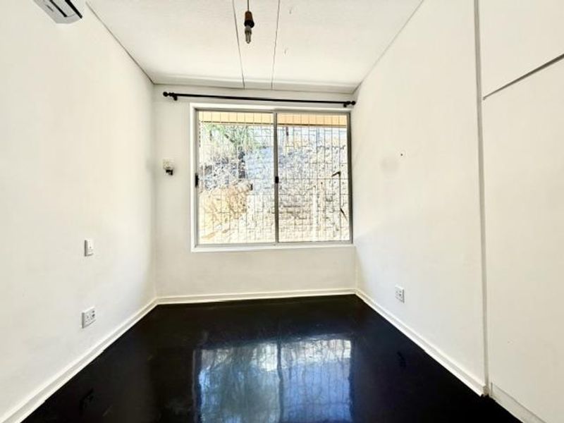 An empty bedroom featuring built-in cupboards, a split-system air conditioner, and a sliding window with security bars.