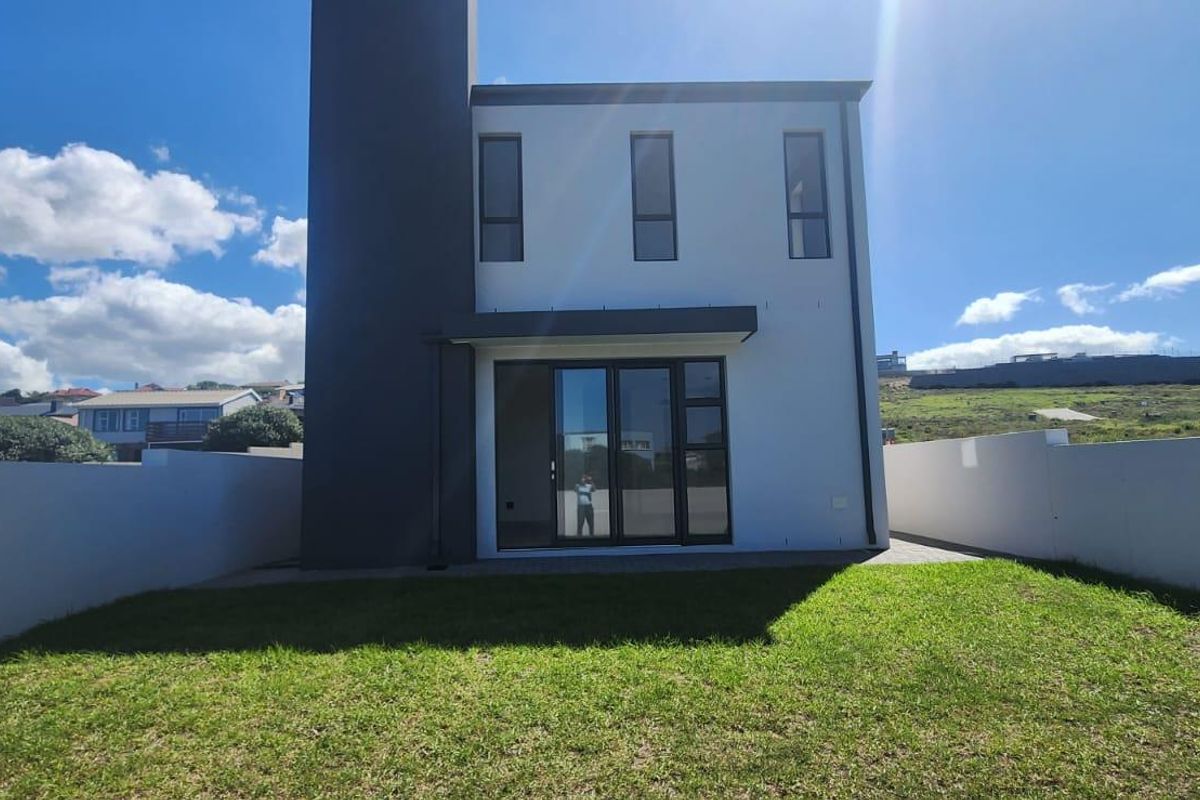 Rear view of a modern two-story townhouse featuring a private lawn, boundary walls, and large glass sliding doors leading to the interior.