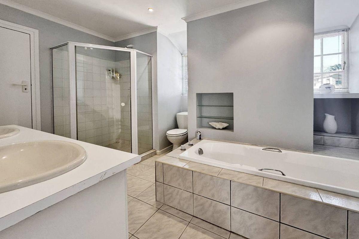 A functional bathroom featuring a built-in bathtub, corner shower enclosure, toilet, and vanity basin with recessed wall shelving.