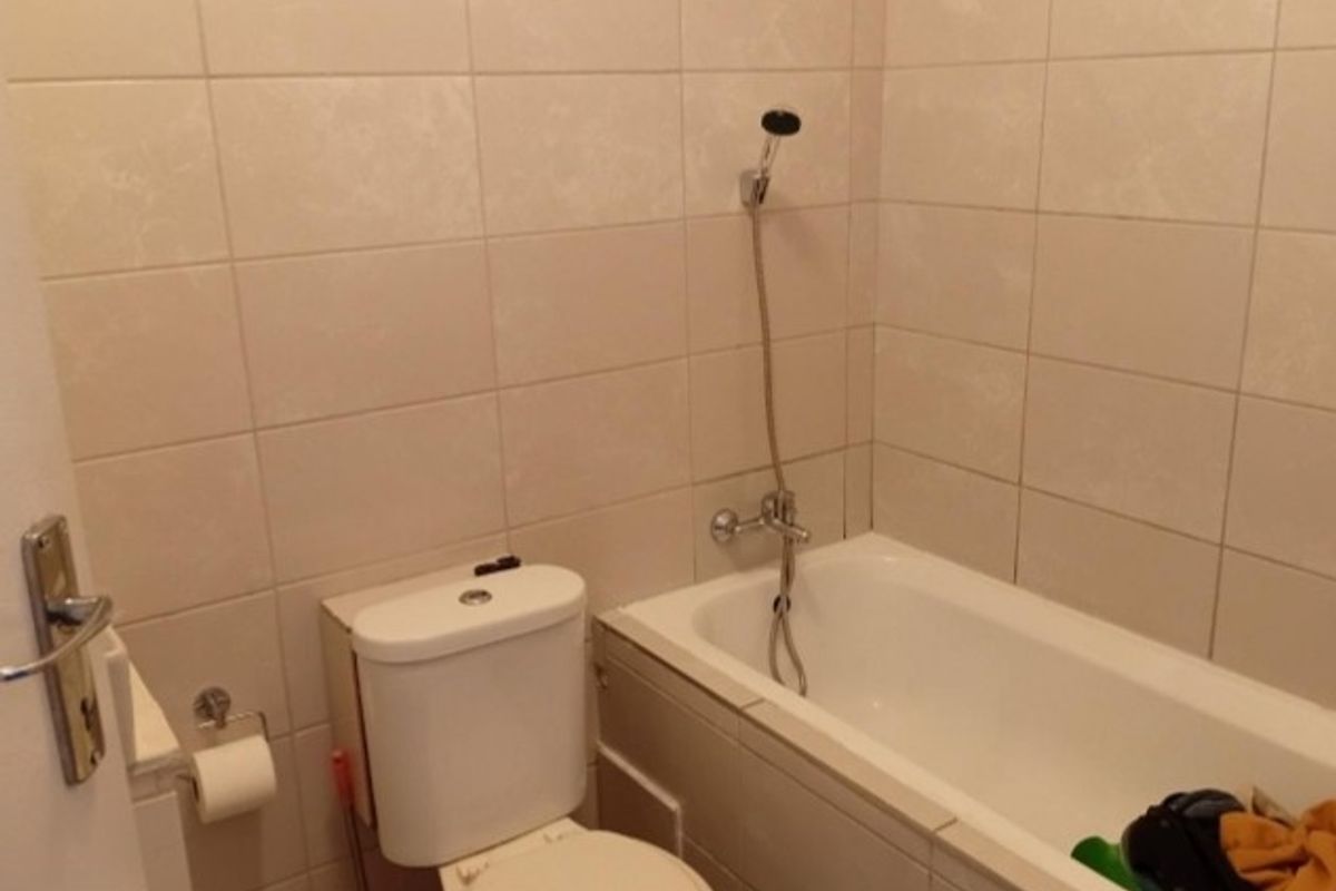 A functional bathroom featuring full-height wall tiling, a standard bathtub with a shower mixer, and a white toilet.