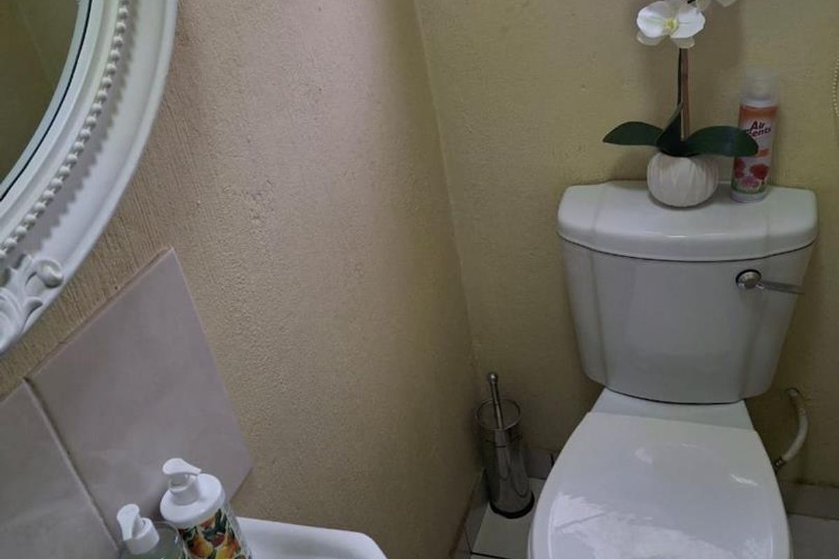 A compact guest bathroom featuring a pedestal basin, toilet, and tiled flooring with security bars on the window.