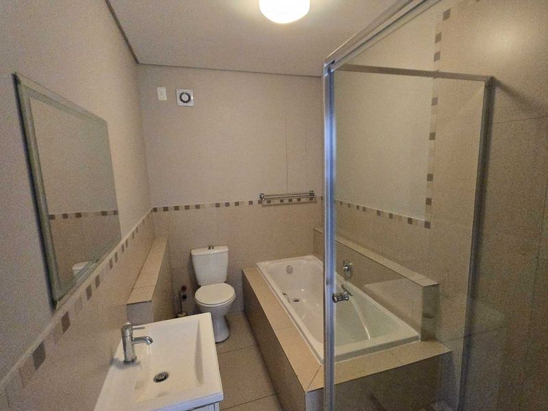 A clean and functional bathroom featuring a built-in bathtub, separate glass shower enclosure, ceramic basin, and neutral wall tiling.
