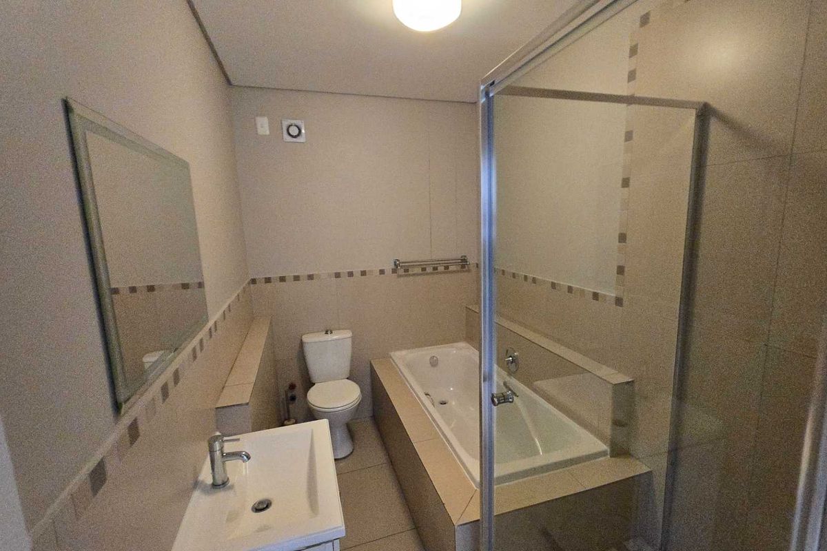 A clean and functional bathroom featuring a built-in bathtub, separate glass shower enclosure, ceramic basin, and neutral wall tiling.