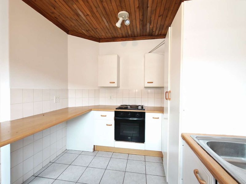 A functional kitchen featuring white cabinetry, laminate countertops, a built-in oven and hob, tiled splashbacks, and a distinctive timber-clad ceiling.