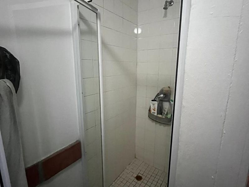 A compact shower stall featuring white wall tiles and a tiled floor, requiring some maintenance and cosmetic updates.