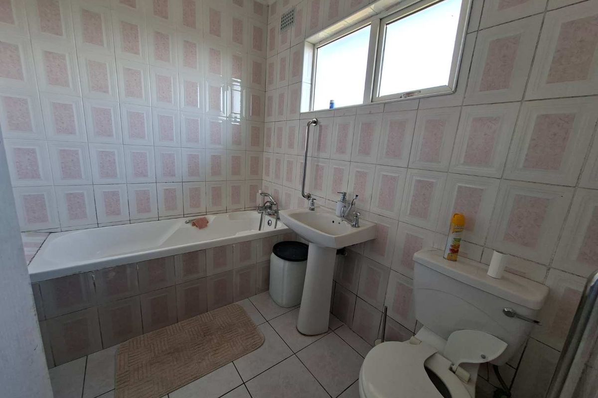 A dated bathroom featuring a bathtub, pedestal sink, and toilet, finished with full-height wall tiling and floor tiles.