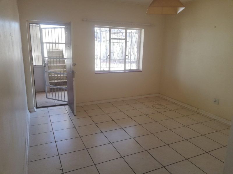 An empty living room featuring tiled flooring, security gate access, and burglar bars on the window, providing a blank canvas for renovation.