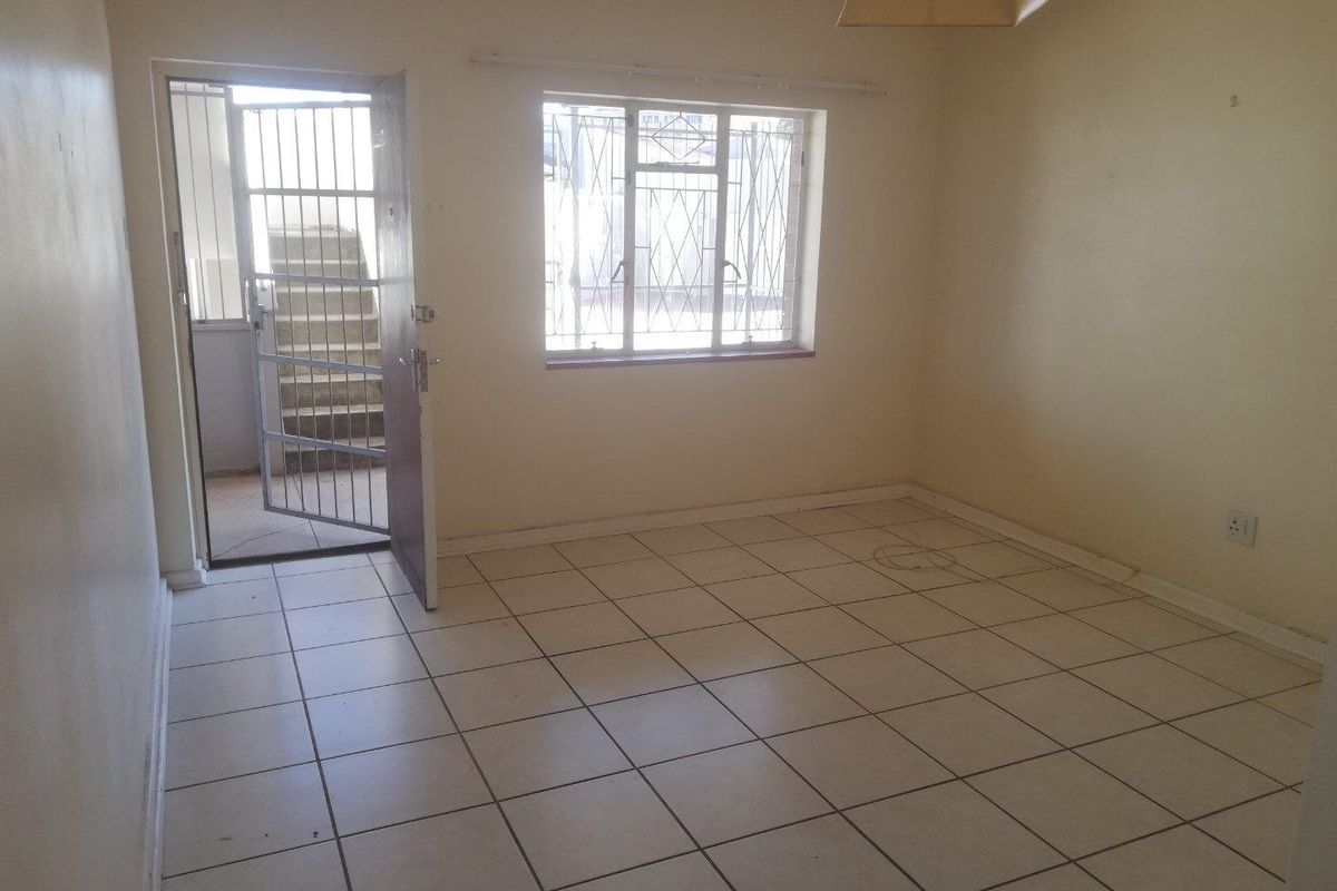 An empty living room featuring tiled flooring, security gate access, and burglar bars on the window, providing a blank canvas for renovation.