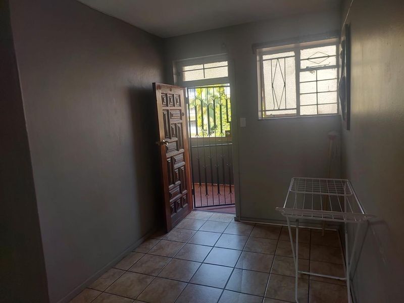A functional entry area featuring tiled flooring, a secure entrance door with a security gate, and natural light through a window with burglar bars.
