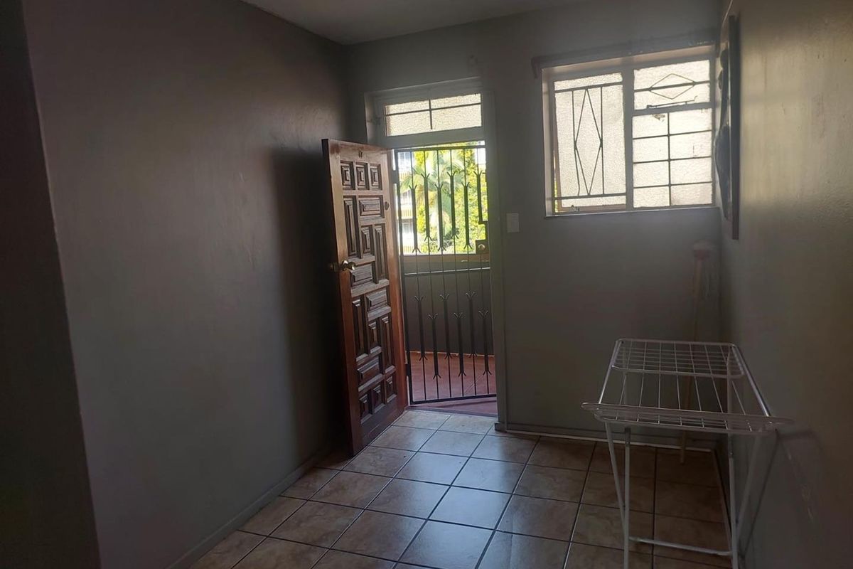 A functional entry area featuring tiled flooring, a secure entrance door with a security gate, and natural light through a window with burglar bars.