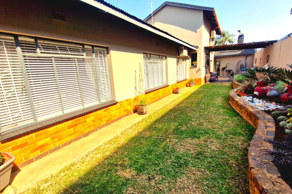 Rear exterior view of the house featuring a well-maintained lawn, raised brick garden beds, and a paved walkway along the building facade.