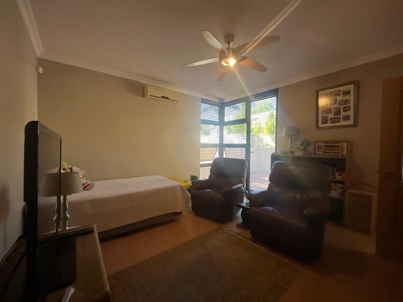 A bedroom featuring laminate flooring, a ceiling fan, and a wall-mounted split-system air conditioner with natural light from a corner window.
