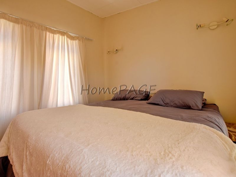 A simple bedroom featuring neutral wall tones, wall-mounted lighting, and window treatments.