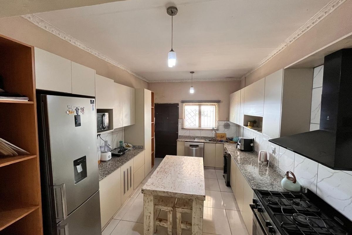 Functional kitchen featuring granite countertops, built-in cabinetry, gas stove with extractor fan, and tiled flooring with a central island.