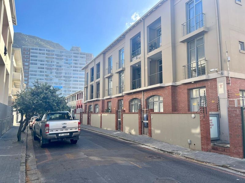 Street view of a multi-story apartment building featuring a brick and render facade with balconies and perimeter security fencing.