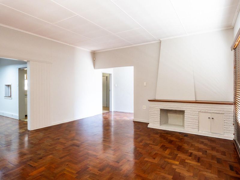 Spacious living room featuring classic parquet flooring, a white brick fireplace with a wooden mantel, and built-in storage cabinetry.