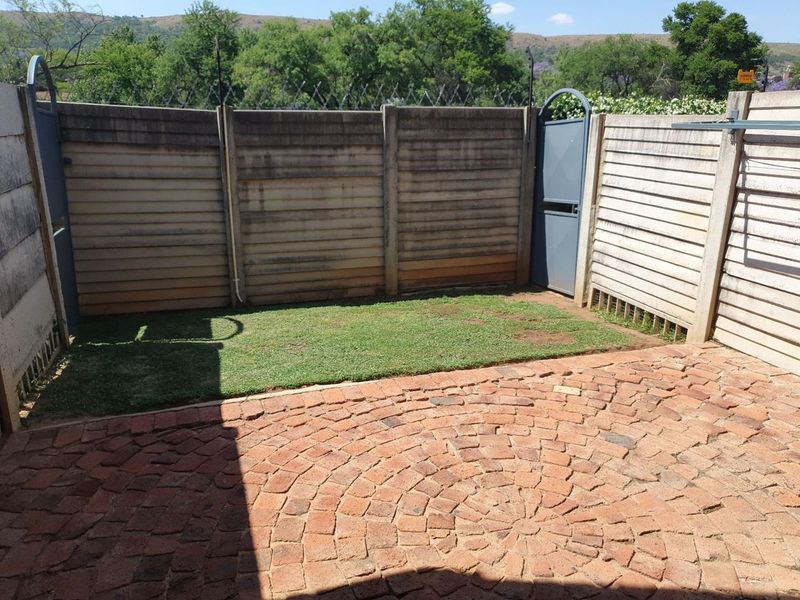 A private rear courtyard featuring a brick-paved patio area, a small lawn, and secure precast concrete boundary walls with security fencing.