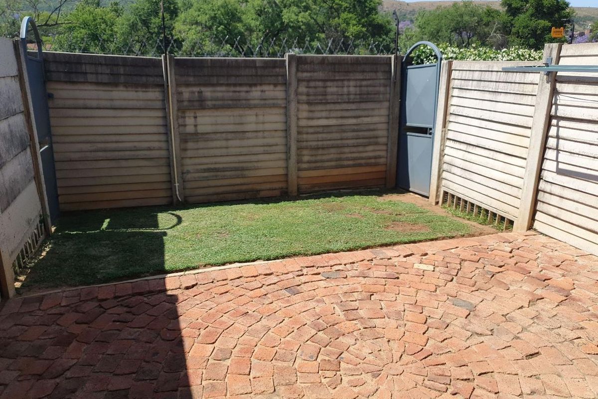 A private rear courtyard featuring a brick-paved patio area, a small lawn, and secure precast concrete boundary walls with security fencing.