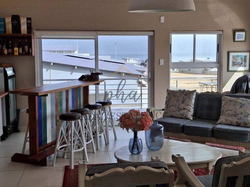 Open plan living area featuring tiled floors, built-in cabinetry, and large sliding glass doors providing access to a balcony with coastal views.