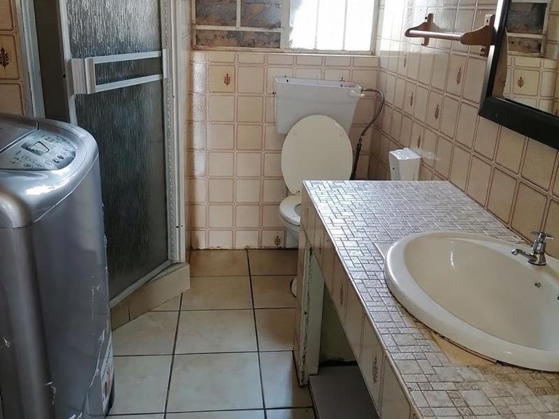 A dated bathroom featuring a tiled vanity, drop-in basin, toilet, and shower enclosure, requiring significant cosmetic updates and repairs to wall finishes.