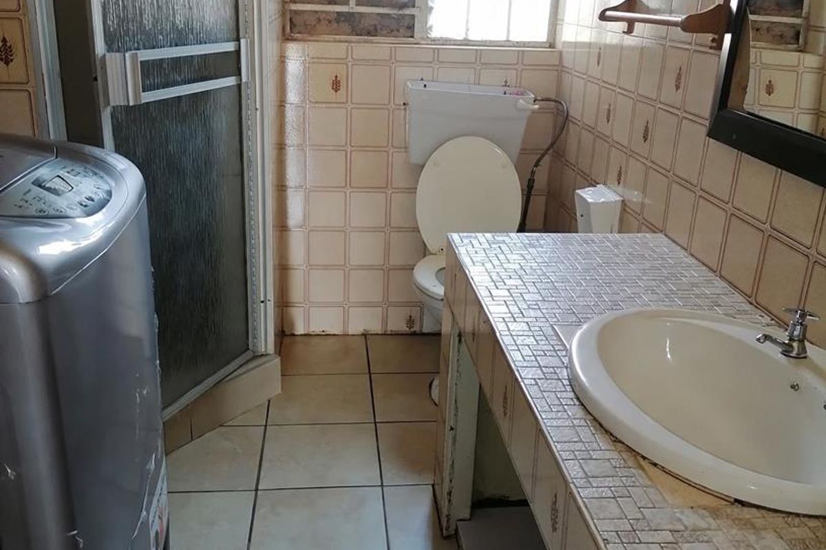 A dated bathroom featuring a tiled vanity, drop-in basin, toilet, and shower enclosure, requiring significant cosmetic updates and repairs to wall finishes.