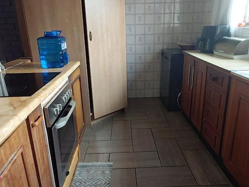 A functional kitchen featuring wooden cabinetry, a built-in oven with hob, extractor fan, and tiled flooring with a neutral backsplash.