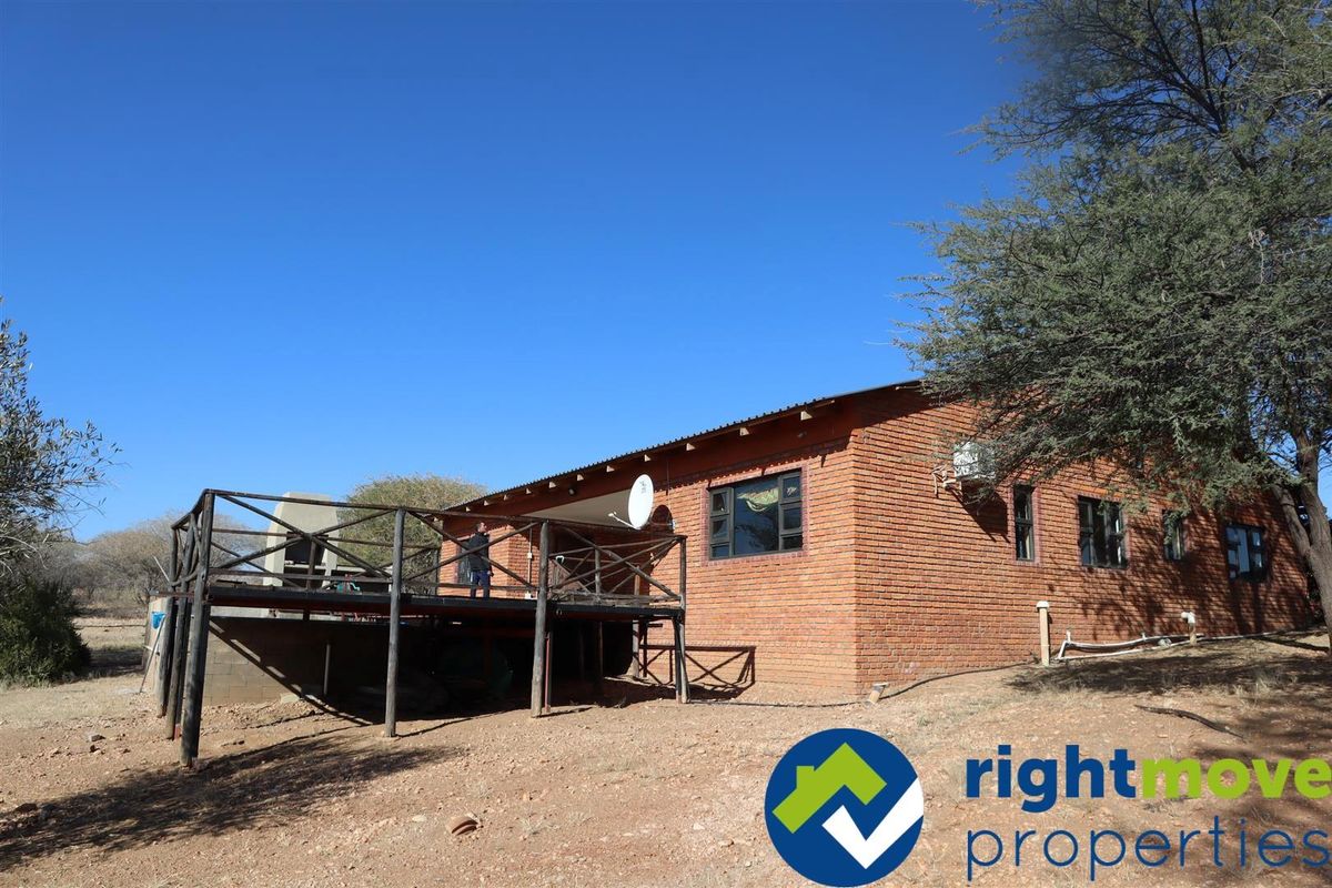 Rear view of a face-brick house featuring an elevated timber deck and outdoor braai area set in a natural landscape.