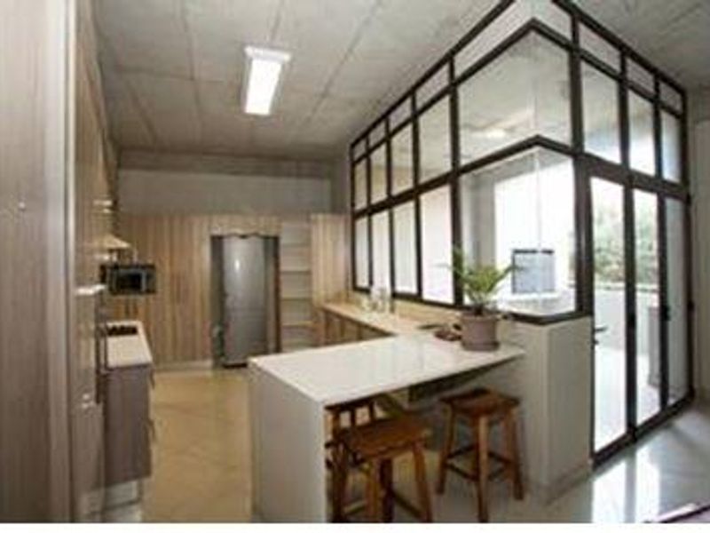 Modern kitchen featuring light wood cabinetry, stone countertops, a breakfast bar, and a stylish glass partition wall with an exposed concrete ceiling.
